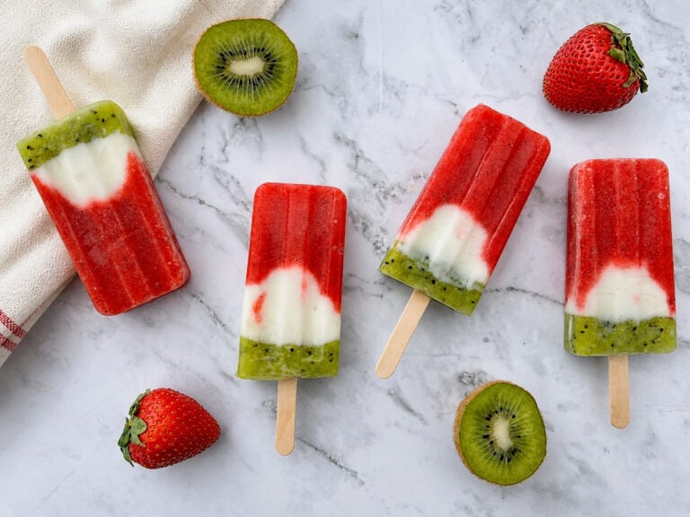 Layered strawberry kiwi popsicles with yogurt on marble surface with fresh fruit