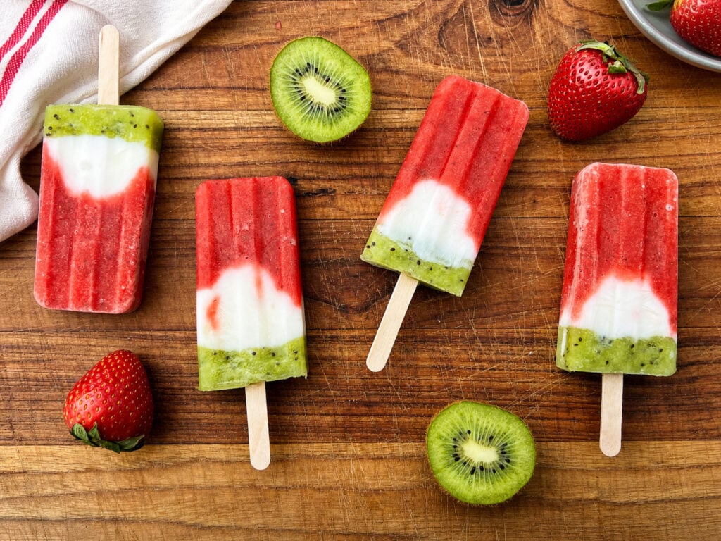 Homemade strawberry kiwi popsicles with yogurt layers served on rustic wooden board