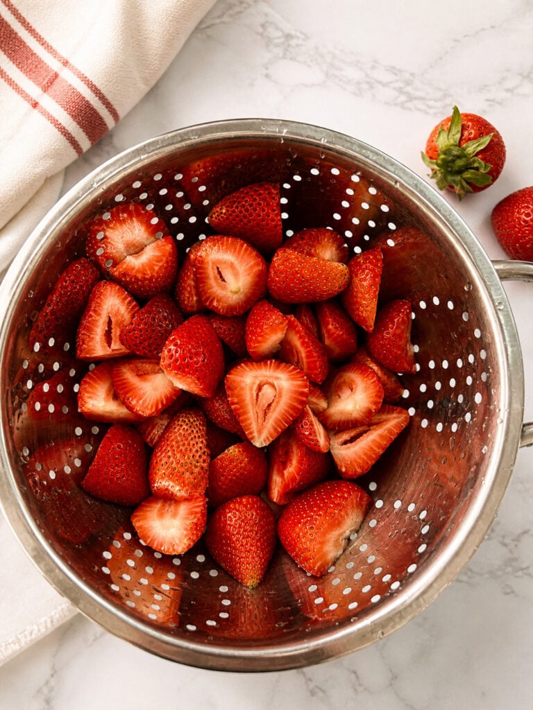 Fresh sliced strawberries in a colander for homemade strawberry kiwi popsicles recipe