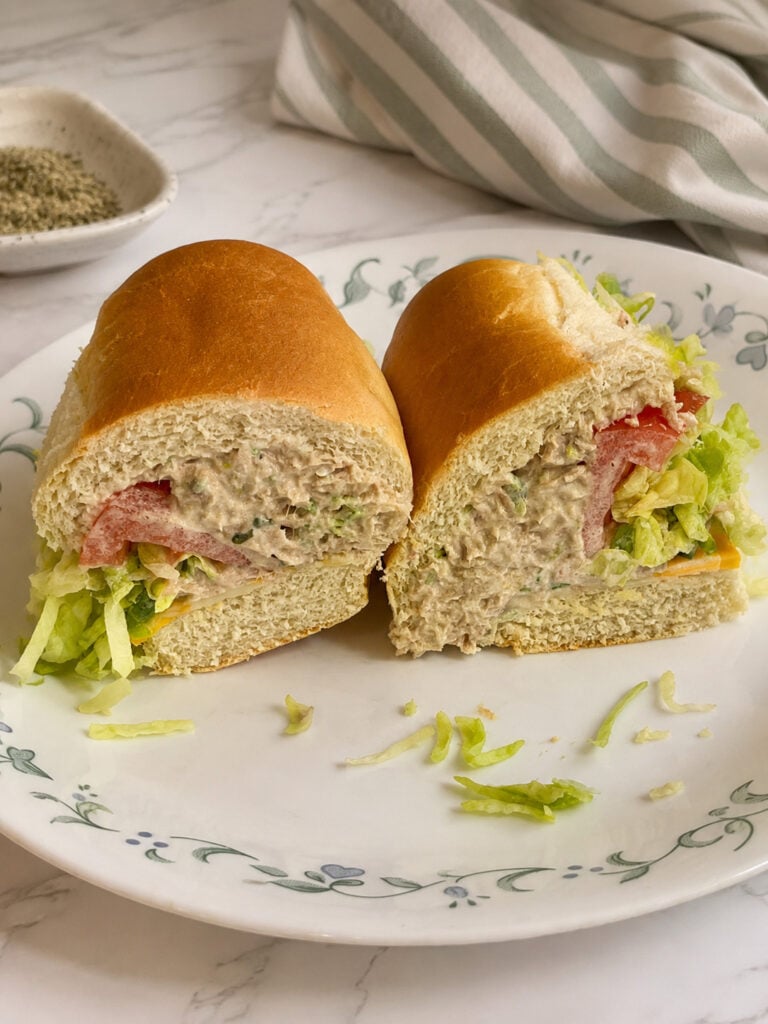 Homemade sandwich served with creamy macaroni salad on a floral plate with shredded lettuce, tomatoes, and soft hoagie bread.