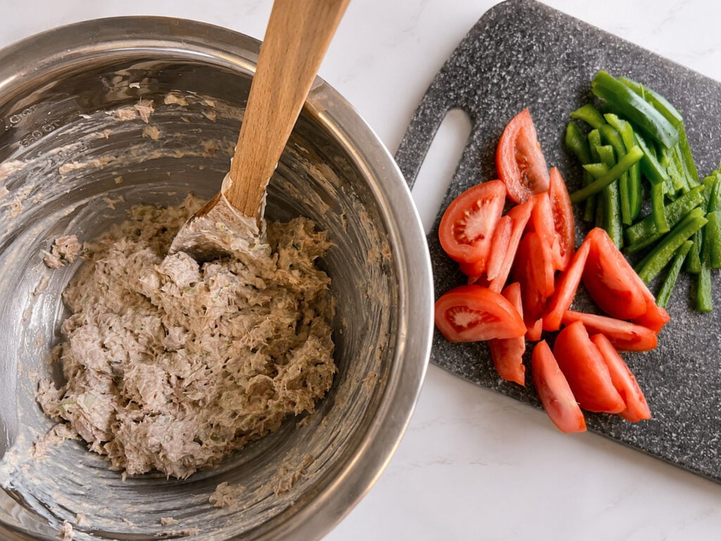Homemade Subway tuna salad filling in a stainless steel bowl beside sliced tomatoes and green peppers for building fresh tuna sub sandwiches.