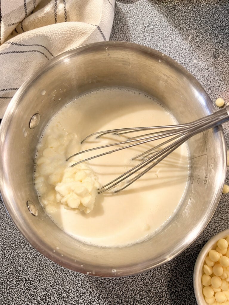 coffee syrup mixture heating in a saucepan with whisk, showing melting white chocolate and cream
