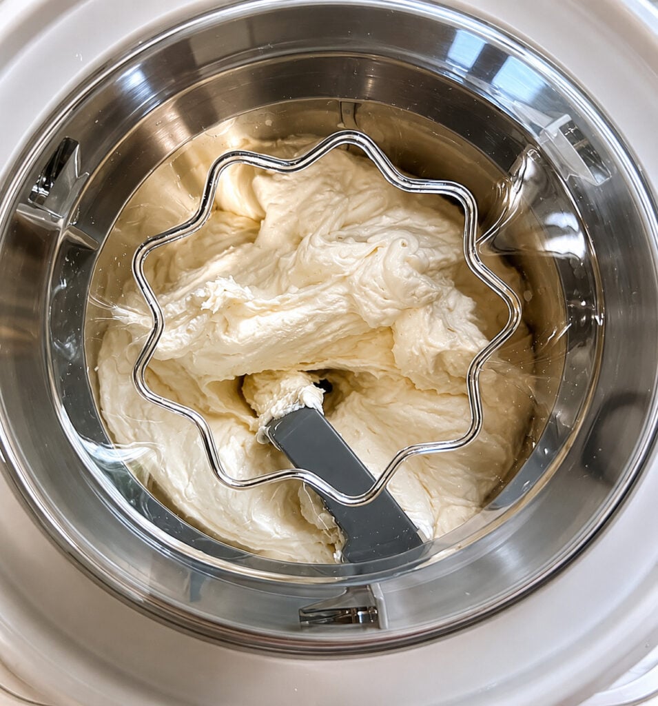 Banana ice cream churning inside an ice cream maker. The creamy homemade ice cream is made with ripe bananas, heavy cream, and brown sugar for a rich frozen dessert.