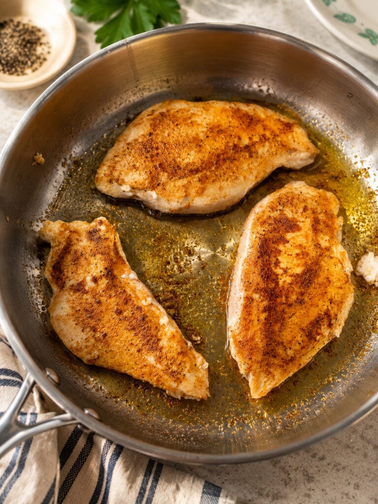Seasoned chicken breasts browning in a skillet with a golden sear, cooking for Bourbon Street chicken.