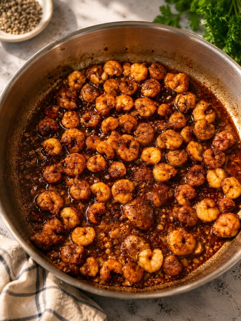 Shrimp simmering in a rich garlic bourbon sauce in a skillet for homemade Bourbon Street chicken and shrimp.