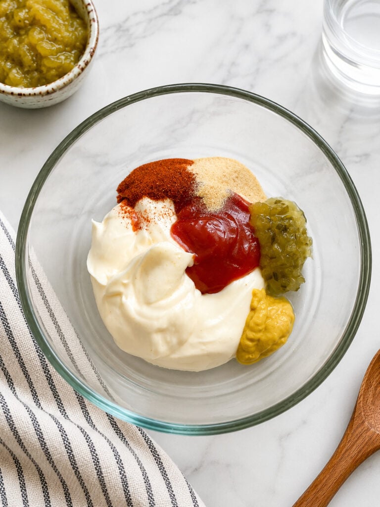 Ingredients for homemade burger bowl sauce including mayonnaise, ketchup, yellow mustard, sweet pickle relish, paprika, garlic powder, and onion powder in a glass mixing bowl.