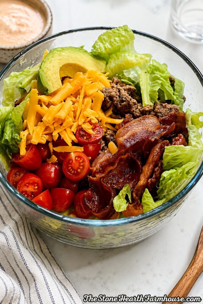 Loaded burger bowl with seasoned ground beef, crispy bacon, cheddar cheese, avocado, cherry tomatoes, romaine lettuce, and homemade burger sauce.