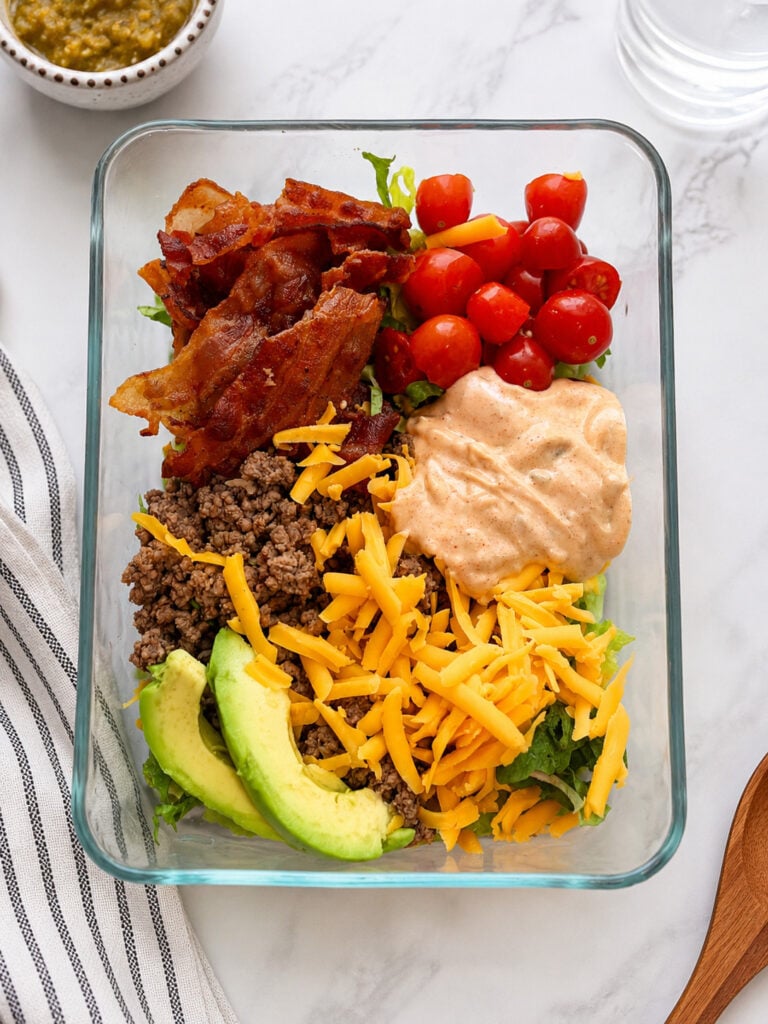Loaded burger bowl with seasoned ground beef, crispy bacon, cheddar cheese, avocado, cherry tomatoes, lettuce, and creamy homemade burger sauce for an easy low-carb cheeseburger bowl recipe.