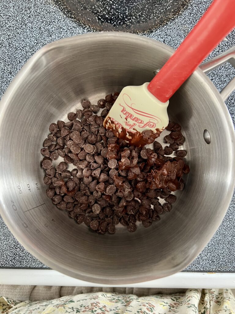 Semi-sweet chocolate chips melting in a saucepan with a silicone spatula for homemade chocolate Rice Krispie bars.