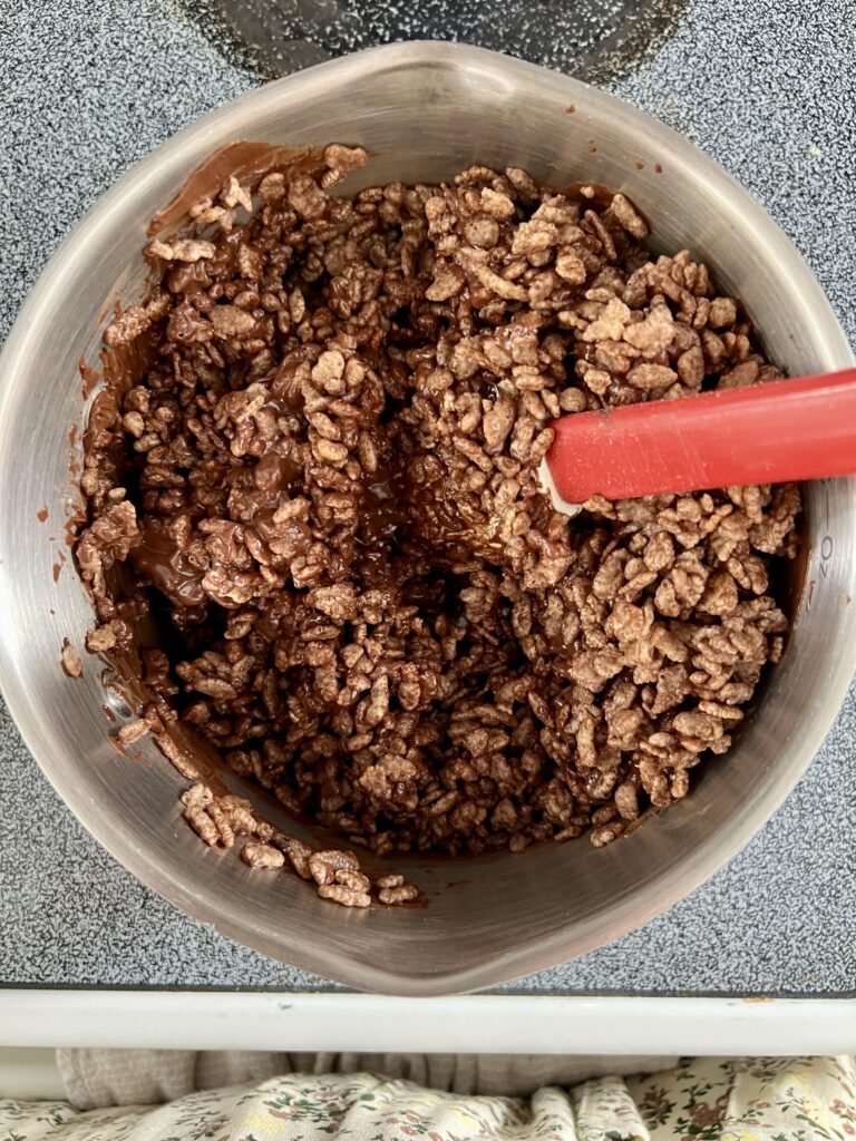 Cocoa Krispies cereal being folded into a melted chocolate peanut butter mixture in a saucepan.