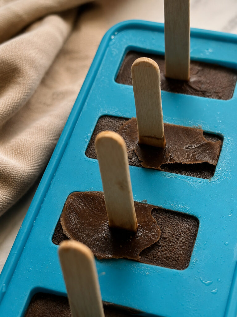 Coffee popsicle mixture poured into a blue silicone popsicle mold with wooden sticks before freezing.