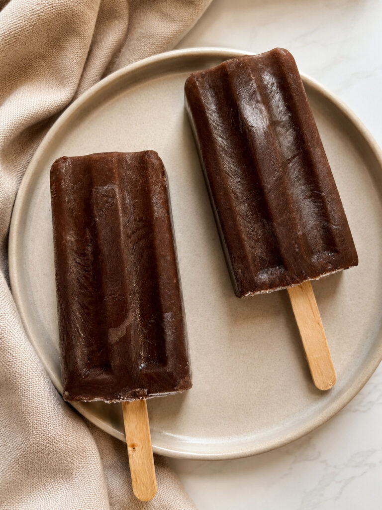 Homemade coffee popsicles on a beige plate with a linen napkin, made with chocolate pudding mix and cold brewed coffee.