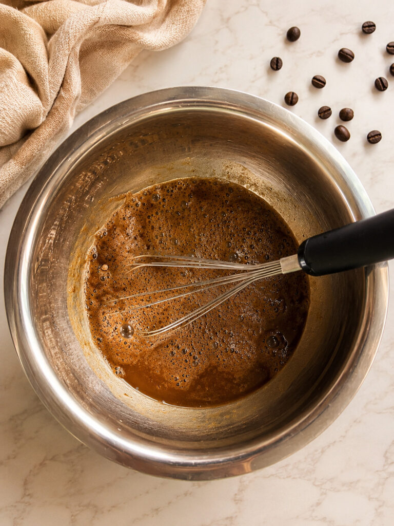 Chocolate pudding and cold coffee mixture being whisked together in a metal bowl to make easy coffee popsicles.