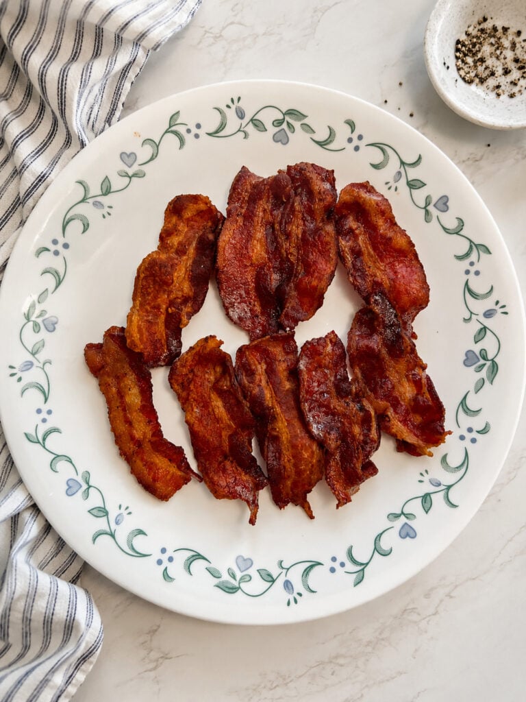 Homemade crispy Instant Pot bacon served on a vintage white plate with a blue-striped kitchen towel.