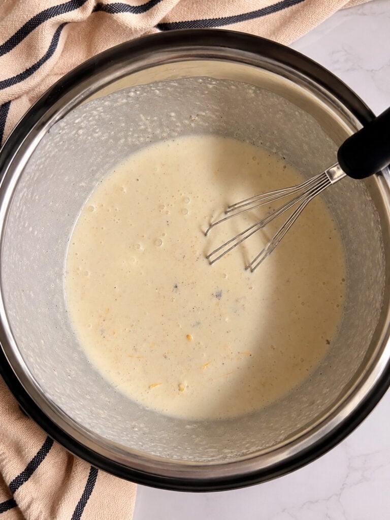 Creamy scalloped potato sauce whisked smooth inside an Instant Pot insert, made with heavy cream, sour cream, cheese, and seasonings.