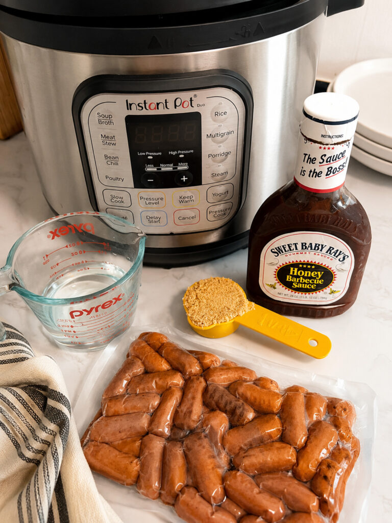 Ingredients for Instant Pot BBQ Little Smokies including cocktail sausages, barbecue sauce, brown sugar, water, and an Instant Pot on a kitchen counter.