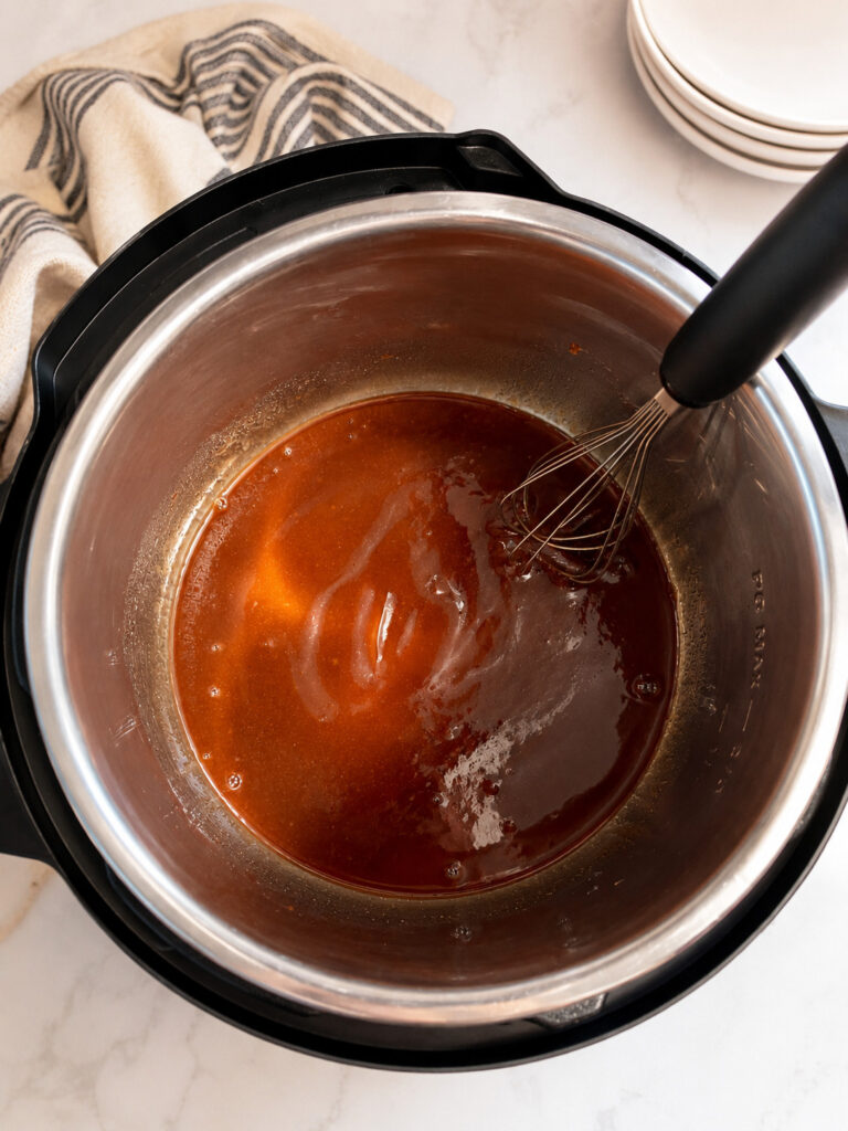 Barbecue sauce mixture being whisked inside an Instant Pot insert before adding Little Smokies cocktail sausages.