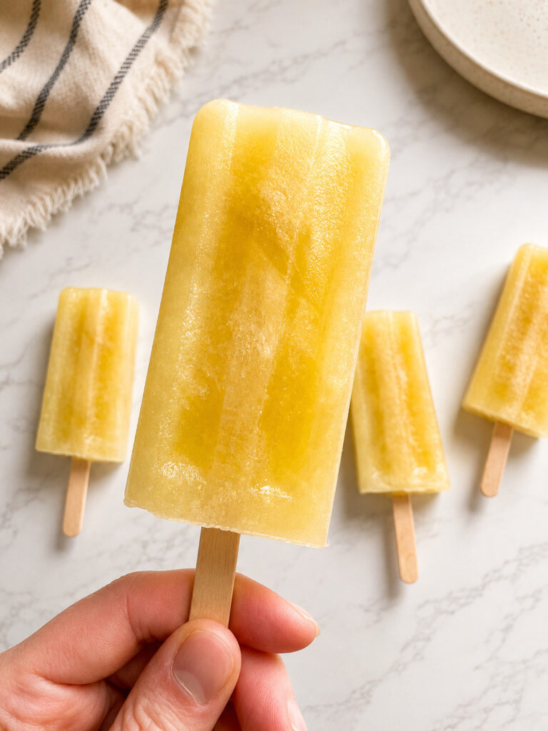 Hand holding a homemade pineapple popsicle made with pineapple juice with additional frozen popsicles in the background.