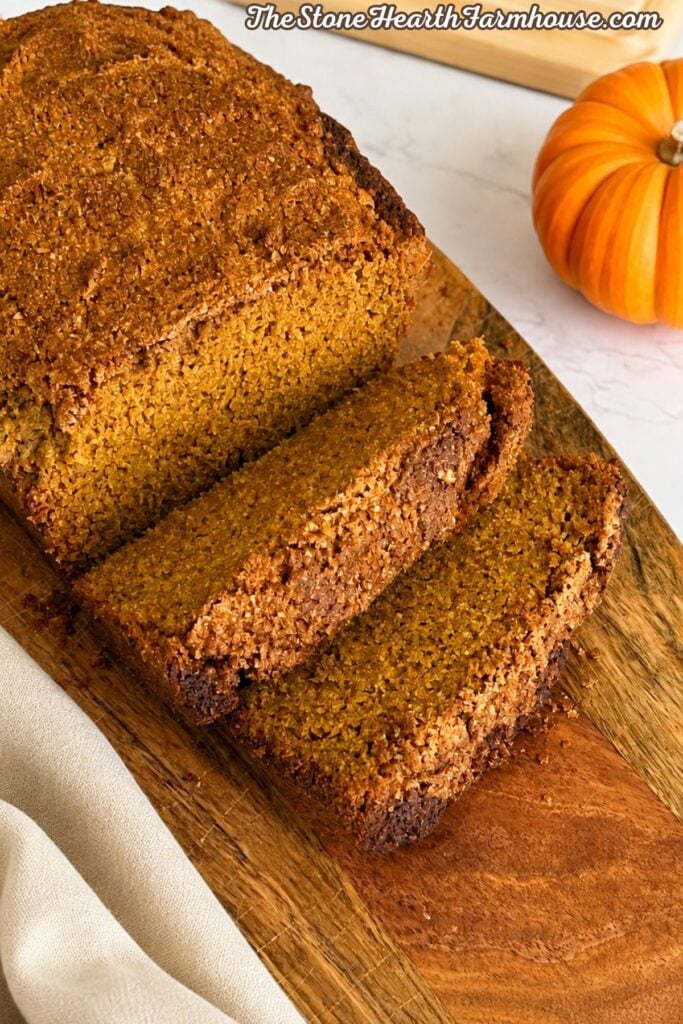 Fresh milled pumpkin bread sliced and served on a wooden board with a pumpkin in the background