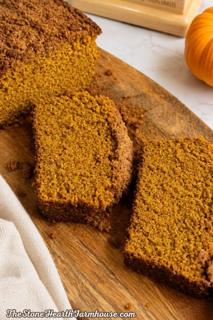 Slices of tender fresh milled pumpkin bread with cinnamon streusel on a wooden cutting board