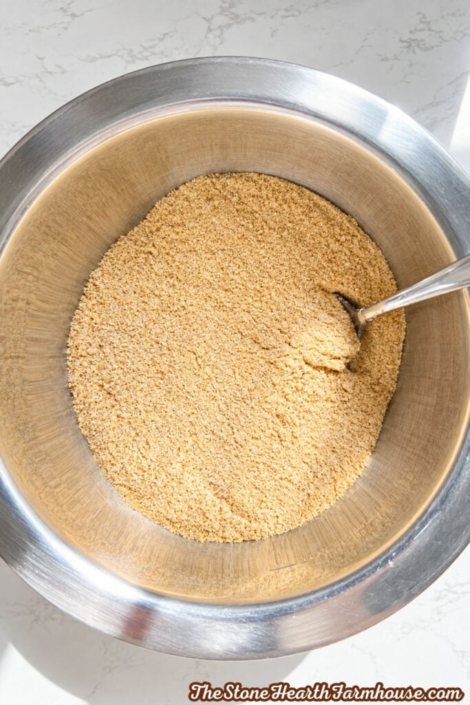 Graham cracker crumbs in a stainless steel mixing bowl for a crust