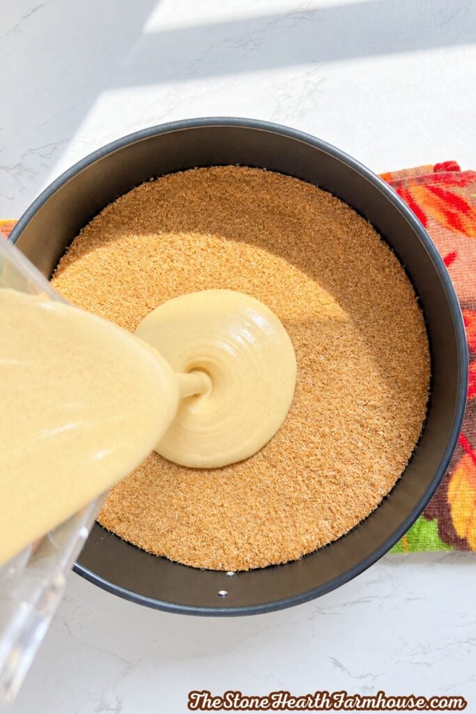 Filling being poured over a graham cracker crust in a springform pan