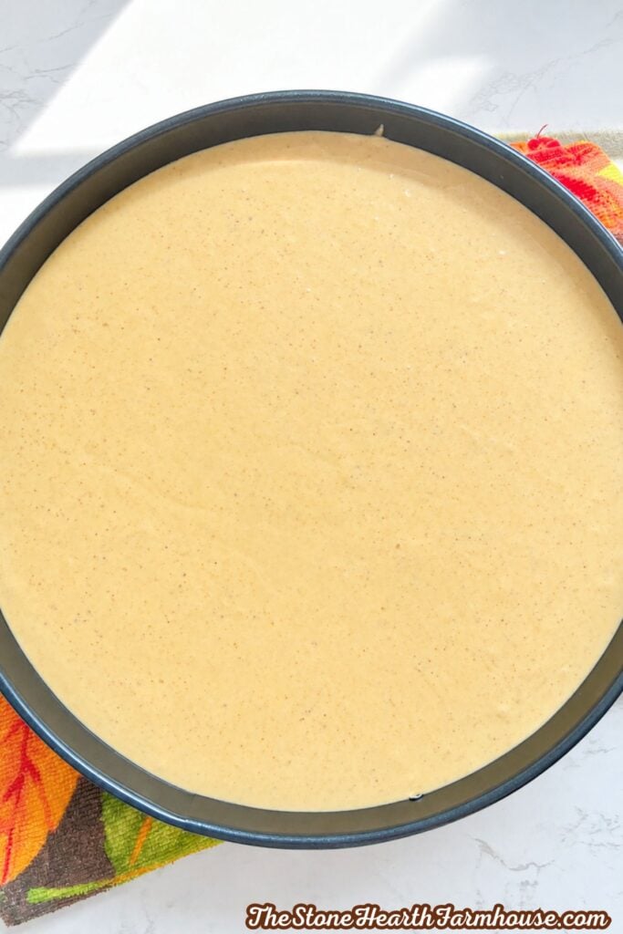 Unbaked pumpkin cheesecake filling spread evenly over the graham cracker crust
