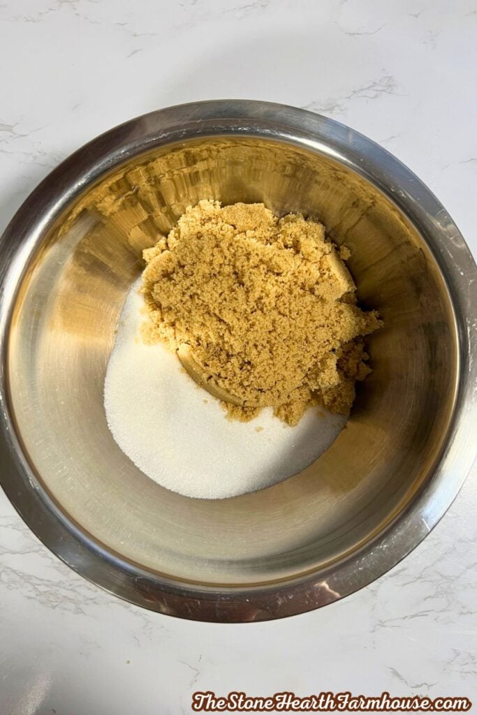 Brown sugar and granulated sugar measured out into a stainless steel bowl. 