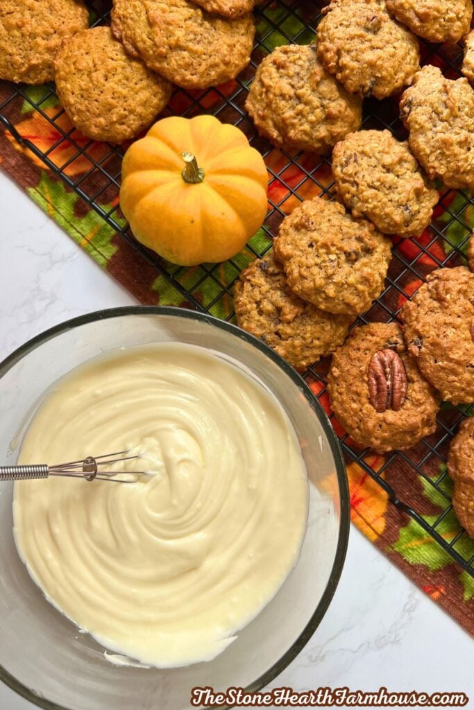 a bowl of cream cheese icing next to the cooking on a cooling rack. 