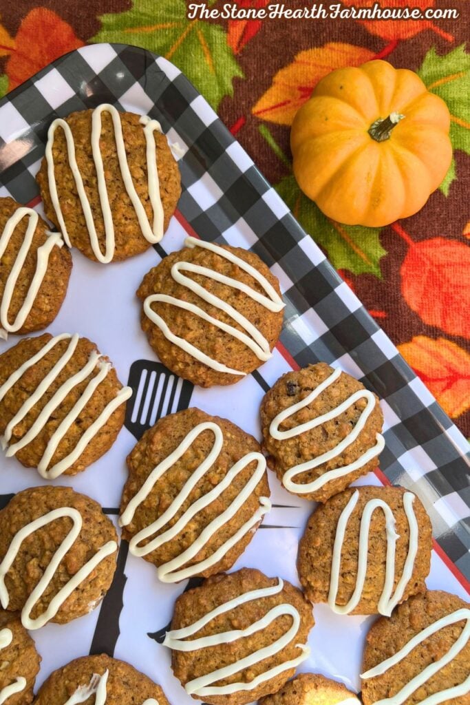 pumpkin cookies on a black and white gingham tray over a fall leaf towel. with cream cheese icing drizzled on top! 