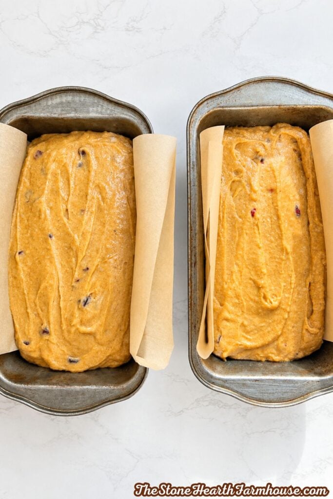 Two loaf pans filled with pumpkin cranberry bread batter ready to bake