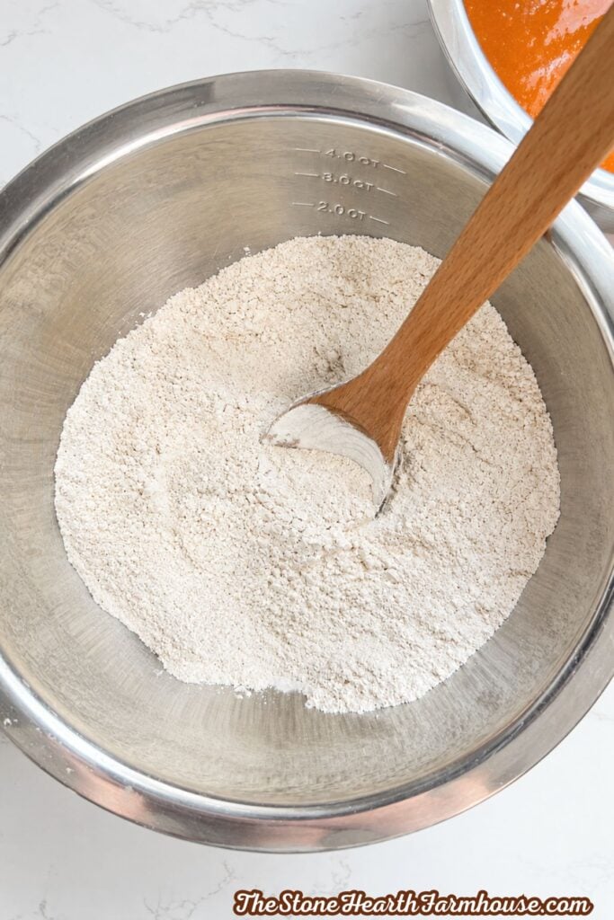 All-purpose flour measured in a stainless steel mixing bowl with a wooden spoon