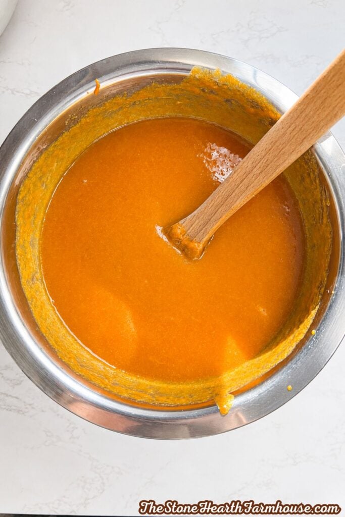 Pumpkin bread batter mixed with pumpkin puree and spices in a stainless steel bowl