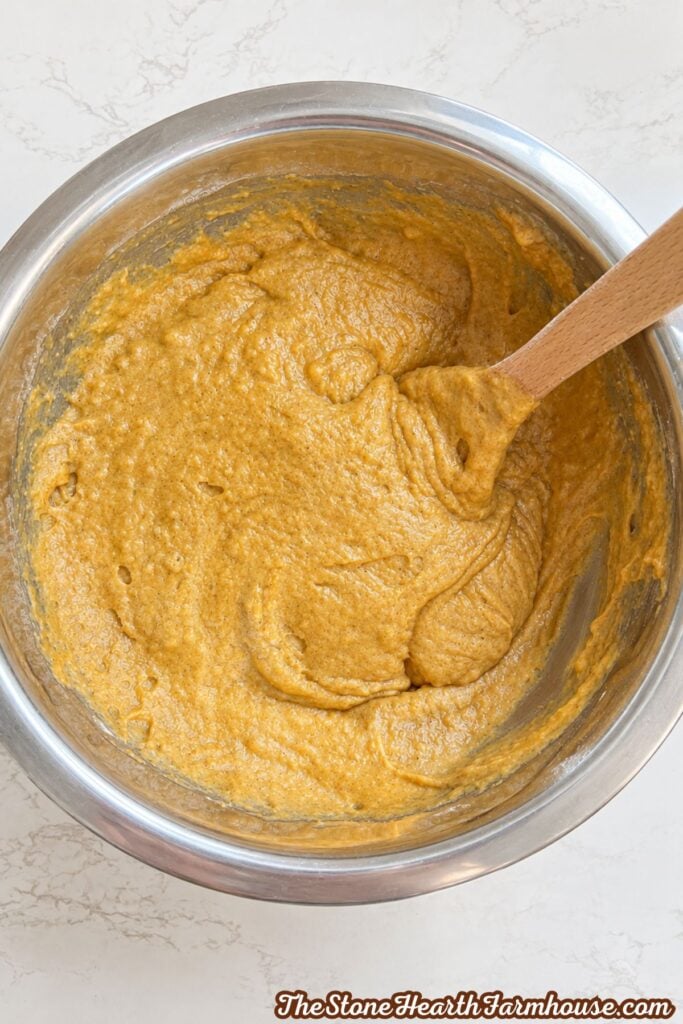 Thick pumpkin bread batter with dried cranberries folded in, stirred with a wooden spoon