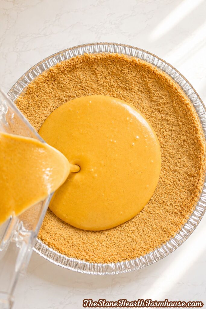 Creamy pumpkin cheesecake mixture being poured into a graham cracker crust