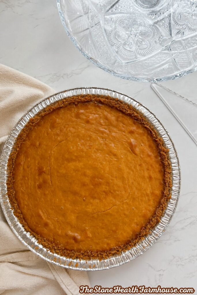 Whole baked pumpkin cheesecake with a golden brown graham cracker crust on a marble countertop