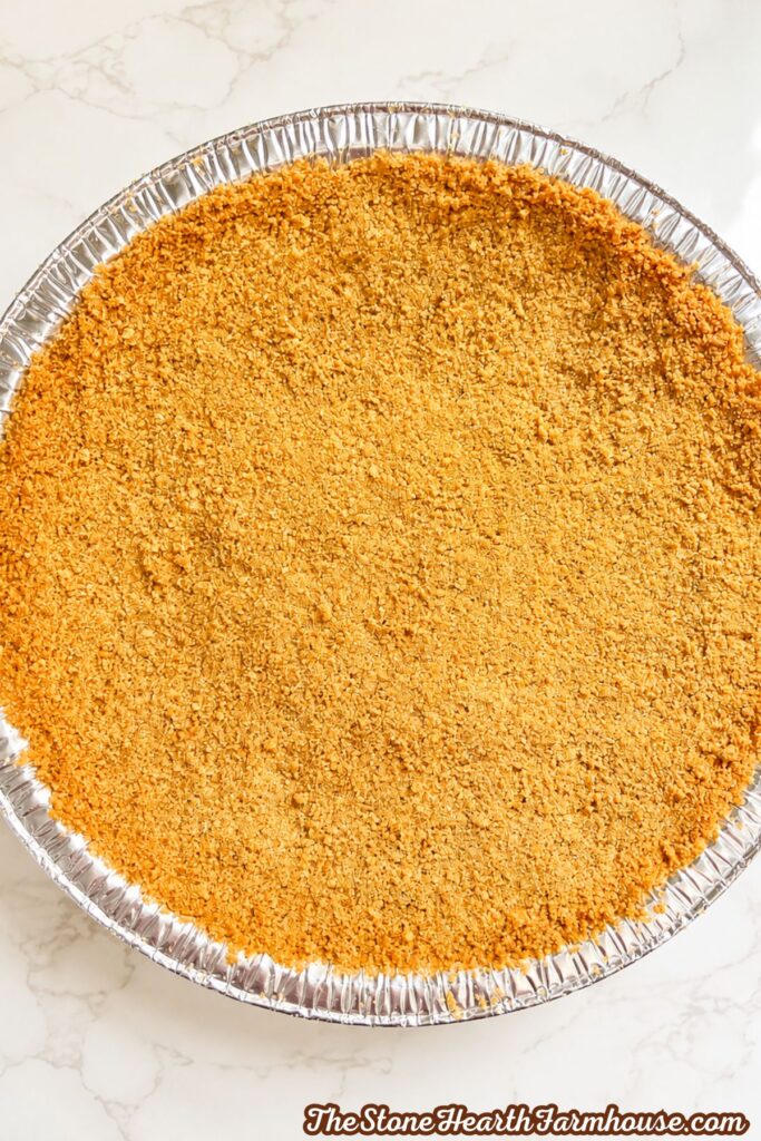 Evenly pressed graham cracker crust filling the bottom of a round pie pan
