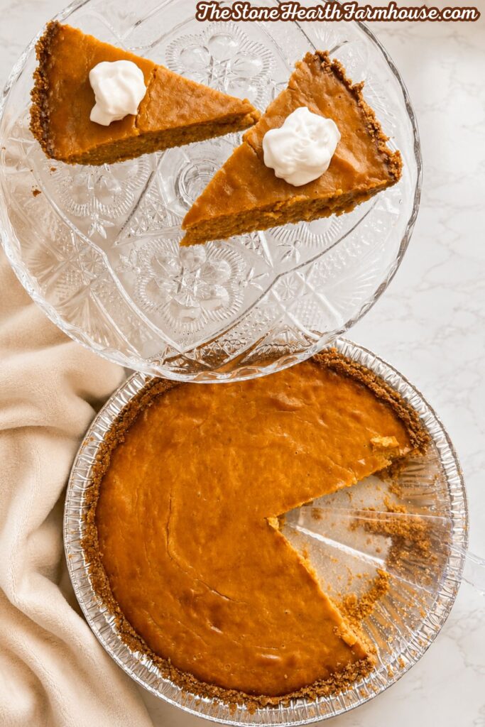 Homemade pumpkin cheesecake pie with a graham cracker crust, sliced and served with whipped cream on a vintage glass cake stand