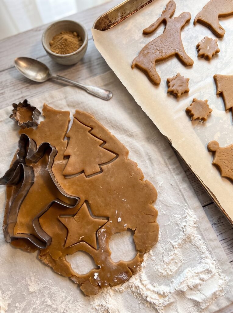 Ginger spice sugar cookie dough rolled out on floured parchment with cutters, tree and star shapes cut, and cookies on a baking sheet